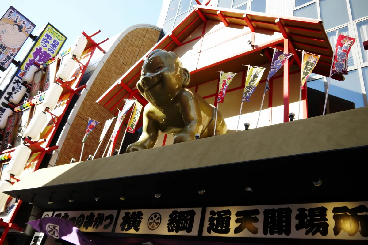 A gilded seated Billiken figure with a pointed head and a wide smile on a red and gold restaurant sign in Osaka