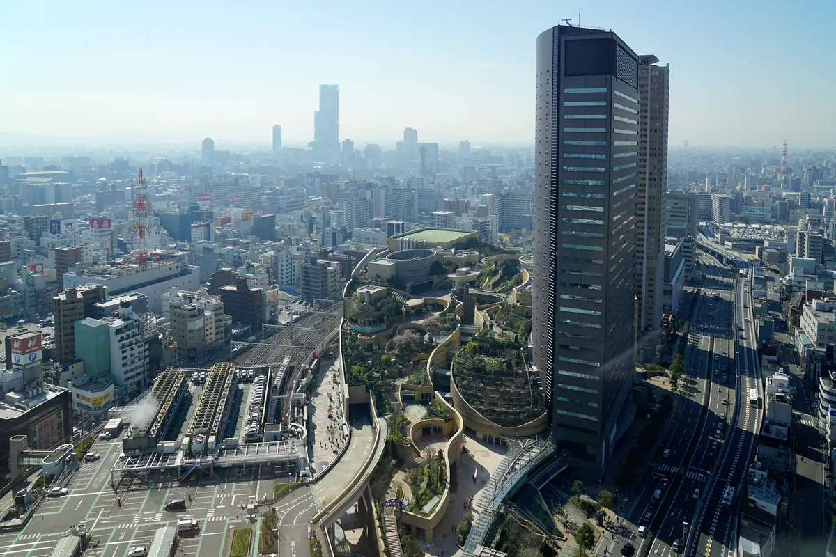 The tall glass tower and terraced roof gardens of the Namba Parks complex seen from above over the city of Osaka